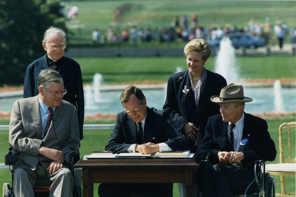 A photo of George H.W. Bush in 1990 signing the ADA on the White House Lawn.